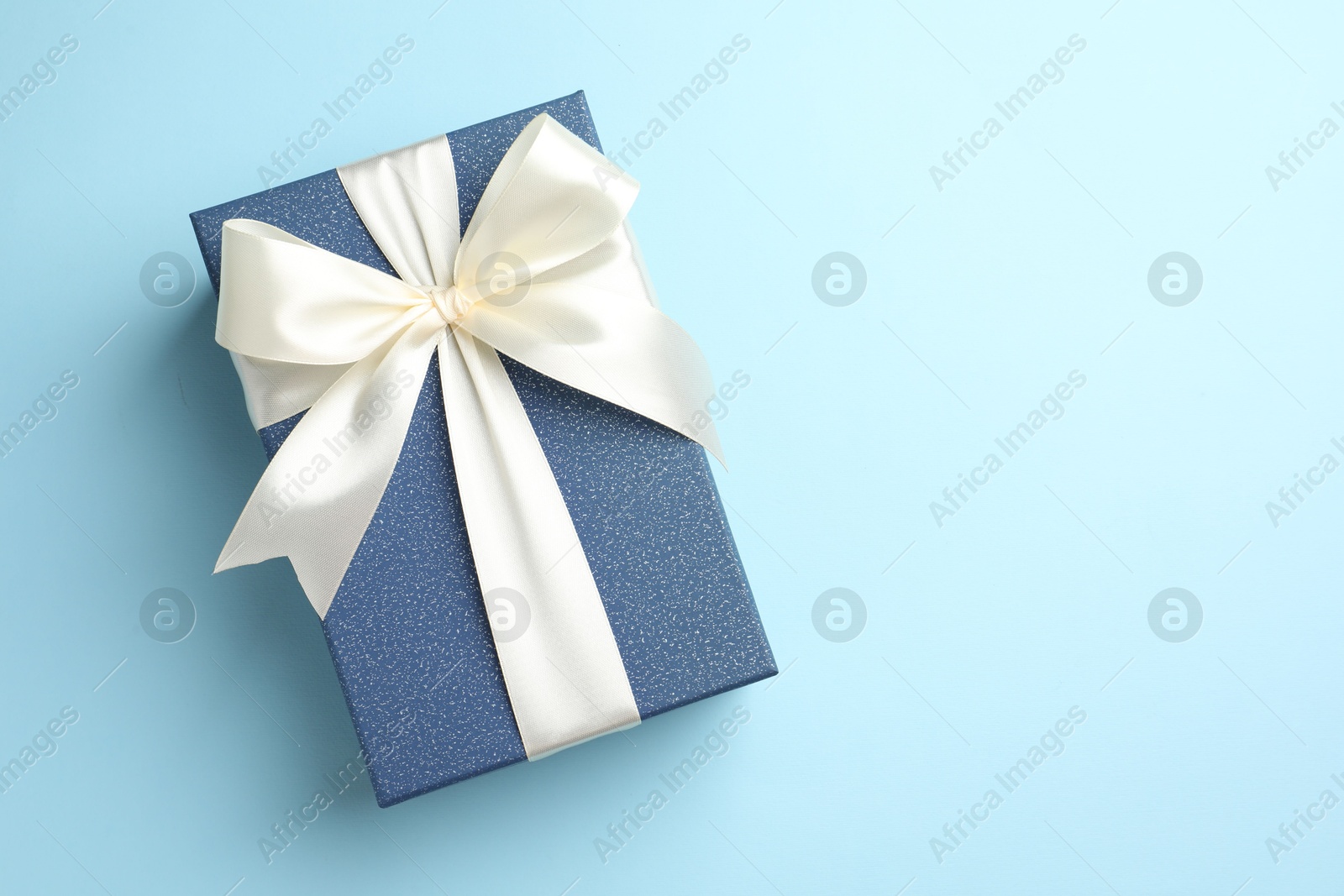 Photo of Gift box with beautiful bow on light blue background, top view. Space for text