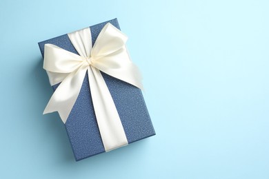 Photo of Gift box with beautiful bow on light blue background, top view. Space for text