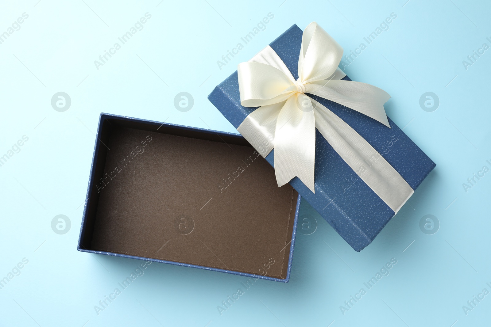 Photo of Opened gift box with beautiful lid on light blue background, top view