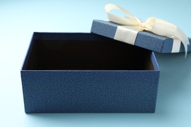 Photo of Opened gift box with beautiful lid on light blue background, closeup