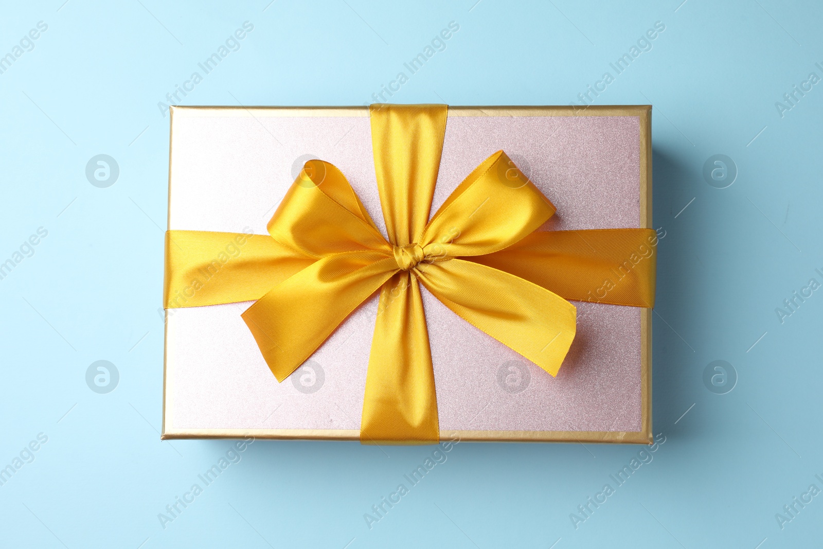 Photo of Gift box with beautiful bow on light blue background, top view
