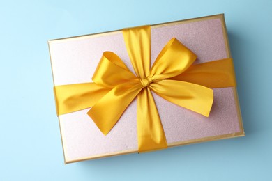 Photo of Gift box with beautiful bow on light blue background, top view