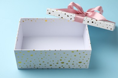 Photo of Opened gift box with beautiful lid on light blue background, closeup