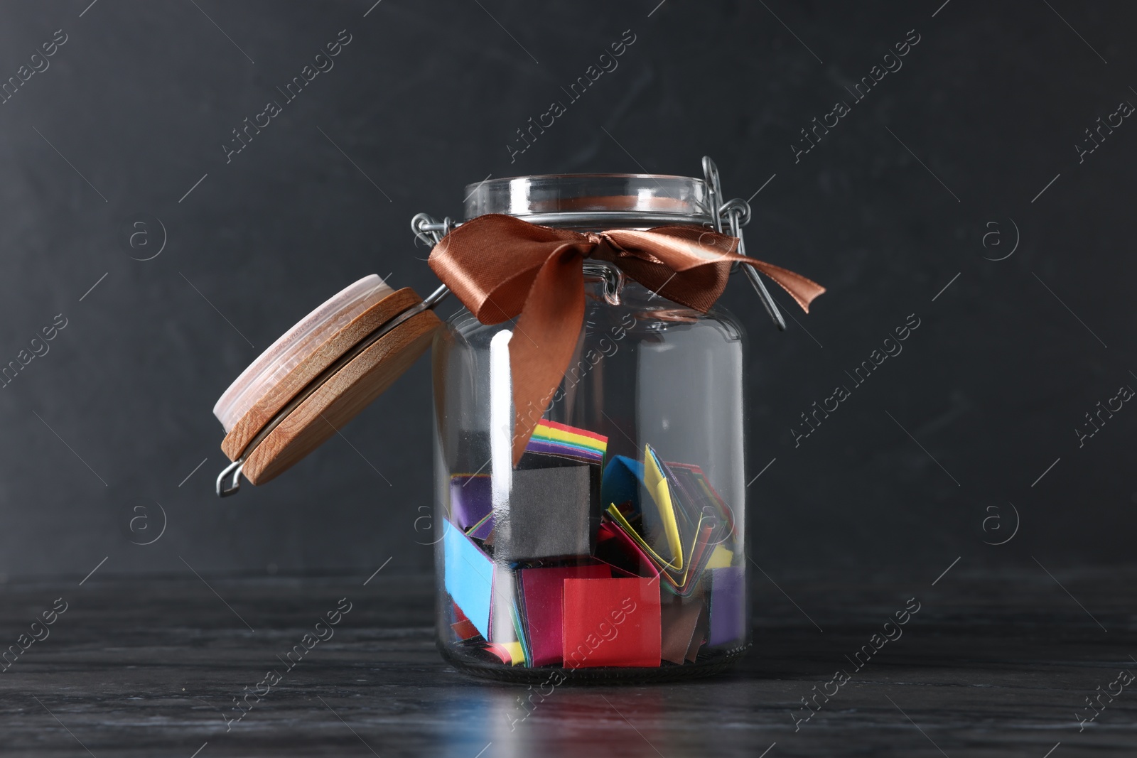 Photo of Colorful paper notes in glass jar with ribbon on black table