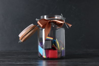 Photo of Colorful paper notes in glass jar with ribbon on black table