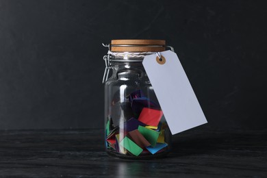 Photo of Colorful paper notes in glass jar with blank card on black table