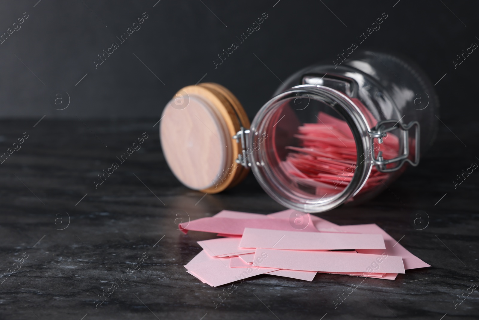 Photo of Pink paper notes in glass jar on black table, closeup. Space for text