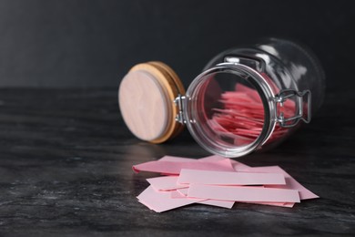 Photo of Pink paper notes in glass jar on black table, closeup. Space for text