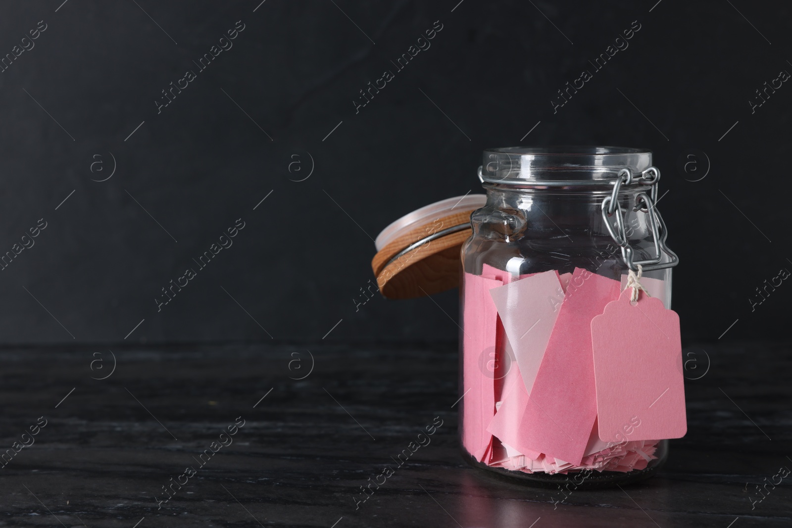 Pink paper notes in glass jar on black table, space for text Photo of Pink paper notes in glass jar on black table, space for text