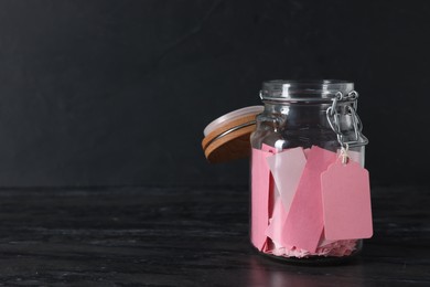 Photo of Pink paper notes in glass jar on black table, space for text