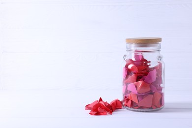 Photo of Colorful paper pieces in glass jar on white table, space for text. Message notes