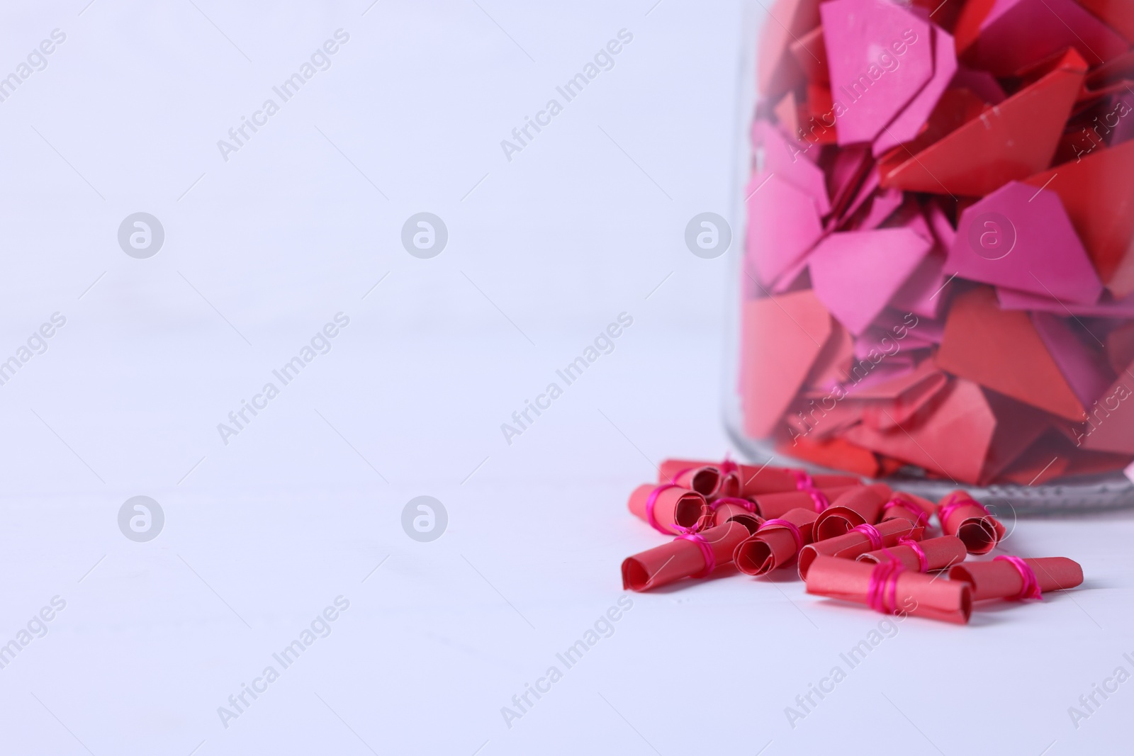 Message notes. Colorful paper pieces in glass jar on white table, closeup. Space for text Photo of Message notes. Colorful paper pieces in glass jar on white table, closeup. Space for text