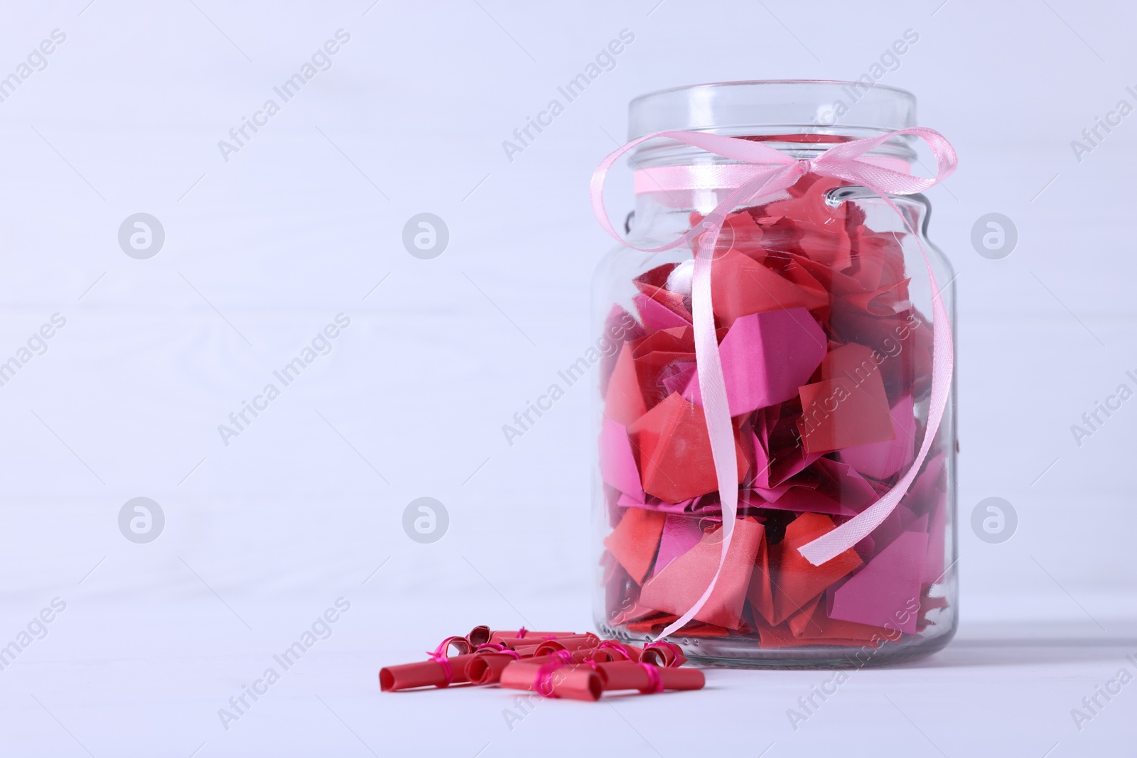 Photo of Colorful paper pieces in glass jar on white table, space for text. Message notes