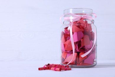 Photo of Colorful paper pieces in glass jar on white table, space for text. Message notes