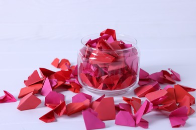 Photo of Colorful paper pieces in glass jar on white table, closeup. Message notes