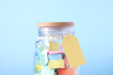 Photo of Colorful paper pieces in glass jar on light blue background, closeup. Message notes