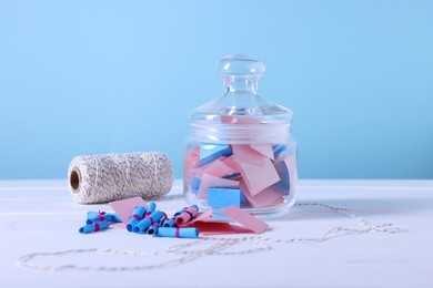 Photo of Colorful paper pieces in glass jar and spool of thread on white wooden table against light blue background