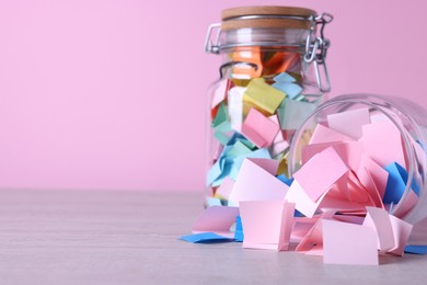 Photo of Message notes. Colorful paper pieces in glass jars on wooden table against pink background, closeup. Space for text
