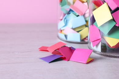 Photo of Message notes. Colorful paper pieces in glass jars on wooden table, closeup. Space for text