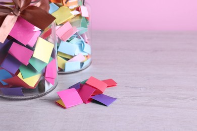 Photo of Message notes. Colorful paper pieces and glass jars on wooden table, closeup. Space for text