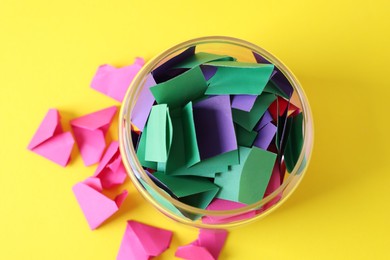 Photo of Colorful paper notes in glass jar on yellow background, top view