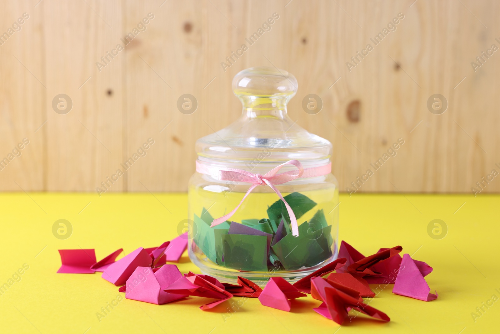 Colorful paper notes and glass jar on yellow table against wooden background, closeup Photo of Colorful paper notes and glass jar on yellow table against wooden background, closeup