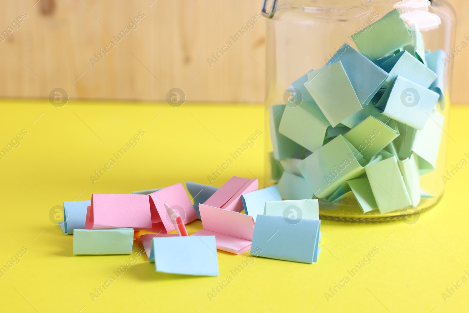 Colorful paper notes in glass jar on yellow table, closeup Photo of Colorful paper notes in glass jar on yellow table, closeup