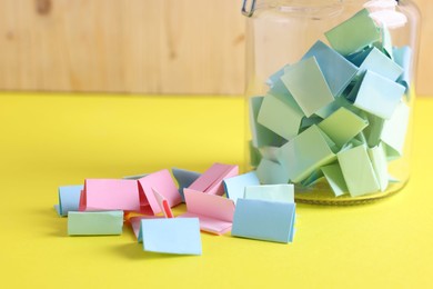 Photo of Colorful paper notes in glass jar on yellow table, closeup
