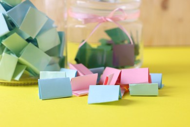 Photo of Colorful paper notes and glass jars on yellow table, closeup