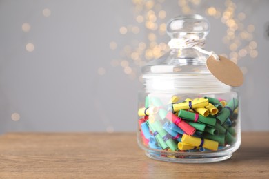 Photo of Colorful paper notes in jar on wooden table against grey background with blurred lights, space for text. Bokeh effect