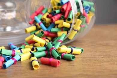 Photo of Colorful paper notes in glass jar on wooden table, closeup. Space for text