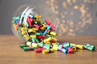 Photo of Colorful paper notes in glass jar on wooden table against grey background with blurred lights, closeup. Bokeh effect