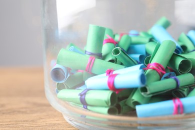 Photo of Colorful paper notes in glass jar on wooden table, closeup