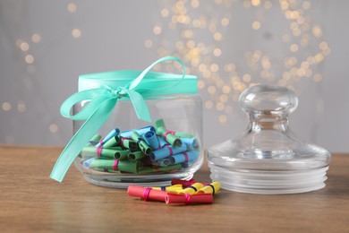 Photo of Colorful paper notes in glass jar on wooden table against grey background with blurred lights, closeup. Bokeh effect