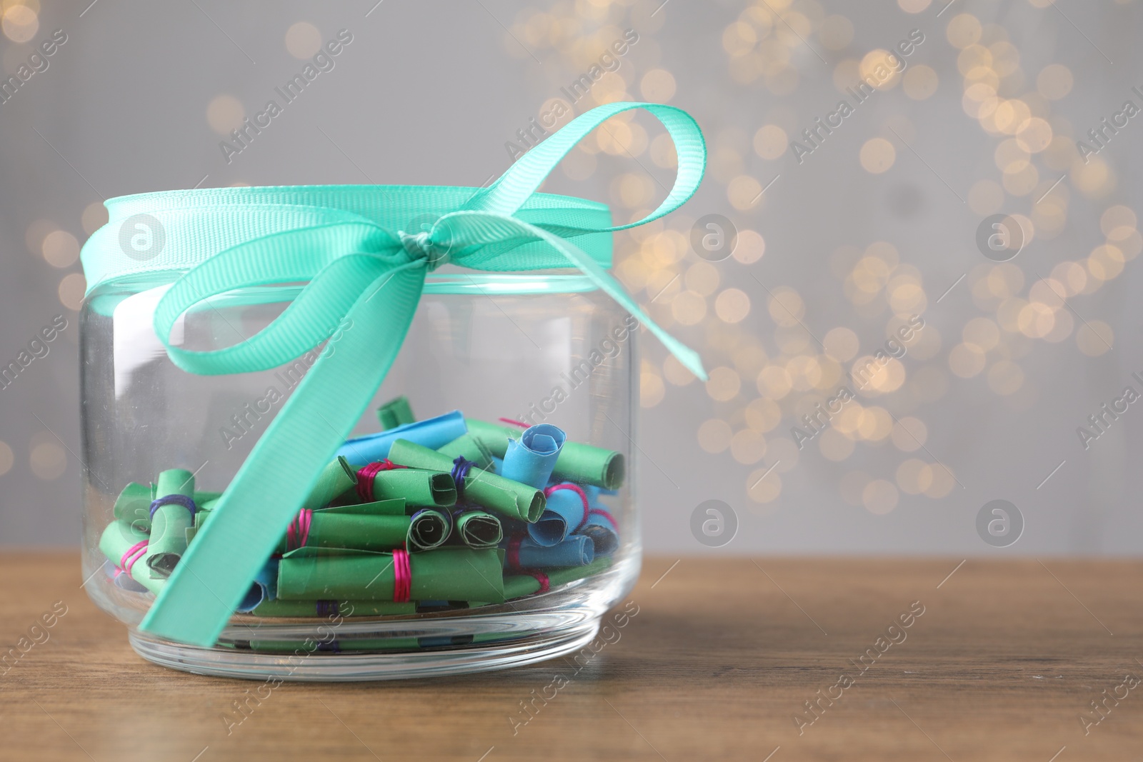 Colorful paper notes in glass jar on wooden table against grey background with blurred lights, space for text. Bokeh effect Photo of Colorful paper notes in glass jar on wooden table against grey background with blurred lights, space for text. Bokeh effect