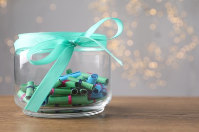 Photo of Colorful paper notes in glass jar on wooden table against grey background with blurred lights, space for text. Bokeh effect