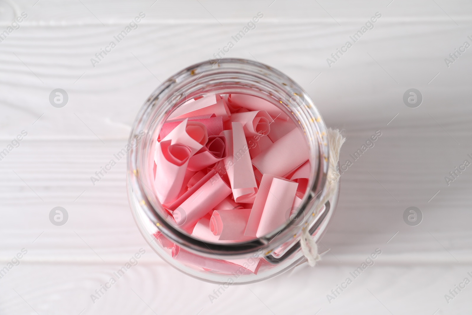 Pink paper notes in glass jar on white wooden table, top view Photo of Pink paper notes in glass jar on white wooden table, top view