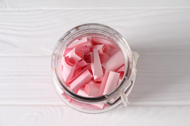 Photo of Pink paper notes in glass jar on white wooden table, top view