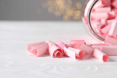 Photo of Pink paper notes in glass jar on white wooden table, closeup. Bokeh effect