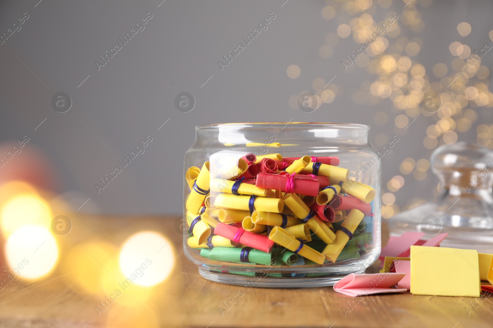 Colorful paper notes in glass jar on wooden table against grey background with blurred lights, space for text. Bokeh effect Photo of Colorful paper notes in glass jar on wooden table against grey background with blurred lights, space for text. Bokeh effect