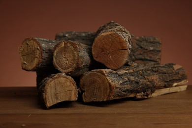 Photo of Pile of cut firewood on wooden table against brown background, closeup