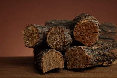 Photo of Pile of cut firewood on wooden table against brown background, closeup
