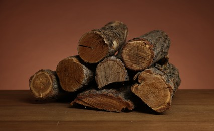 Photo of Pile of cut firewood on wooden table against brown background, closeup