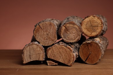 Photo of Pile of cut firewood on wooden table against brown background, closeup