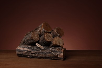 Photo of Pile of cut firewood on wooden table against brown background. Space for text