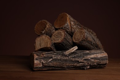 Photo of Pile of cut firewood on wooden table against dark background, closeup