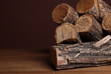 Photo of Pile of cut firewood on wooden table against brown background, closeup. Space for text