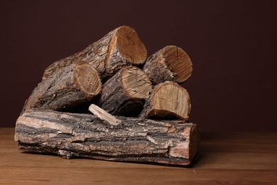 Photo of Pile of cut firewood on wooden table against brown background, closeup