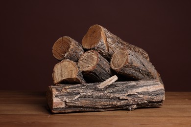 Photo of Pile of cut firewood on wooden table against brown background, closeup