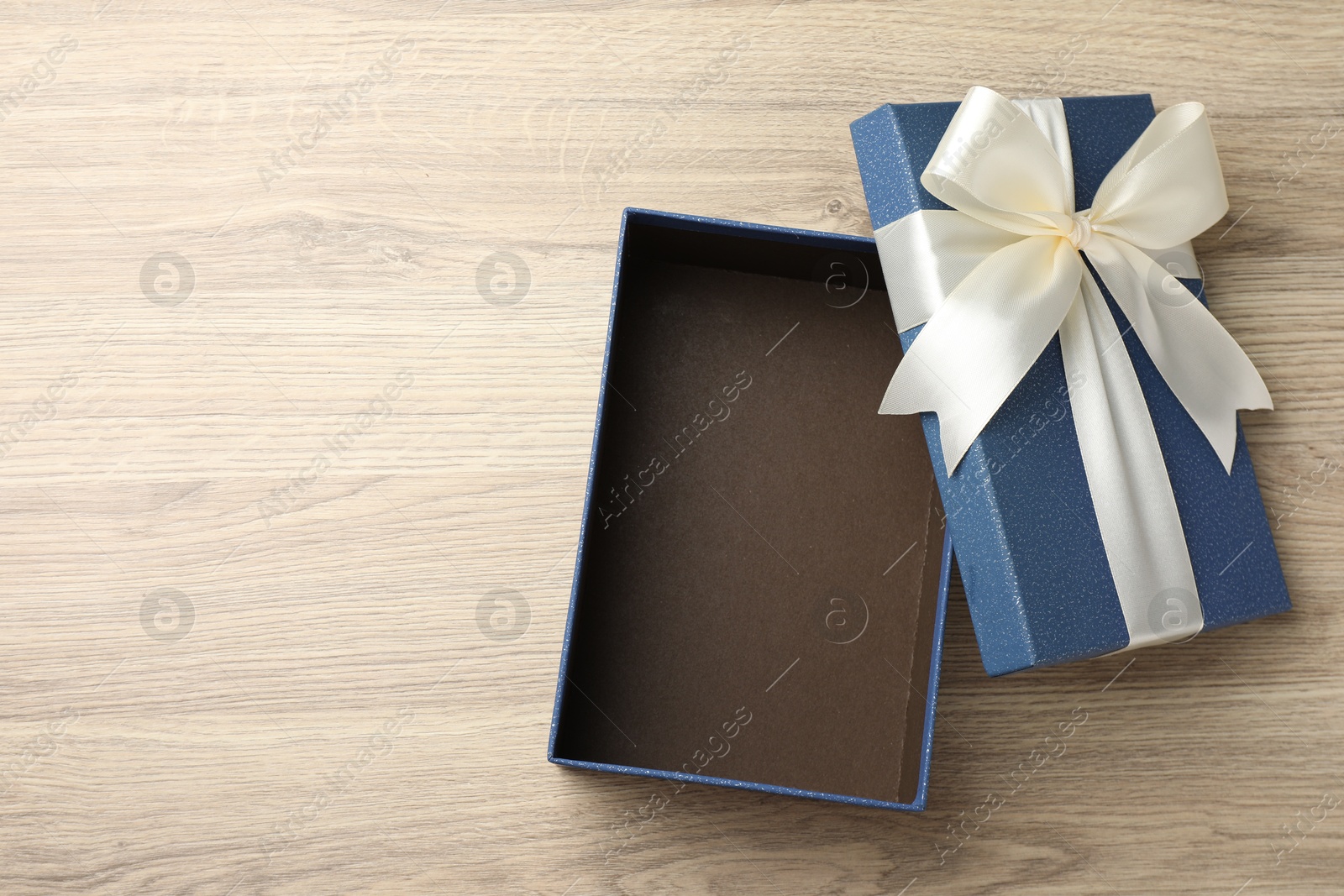 Photo of Opened gift box with beautiful lid on light wooden table, top view. Space for text